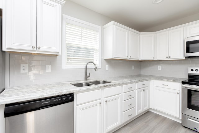 kitchen featuring a sink, backsplash, white cabinetry, light wood-style floors, and appliances with stainless steel finishes