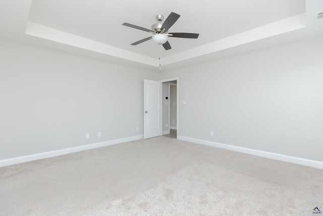 empty room with visible vents, baseboards, ceiling fan, light carpet, and a raised ceiling