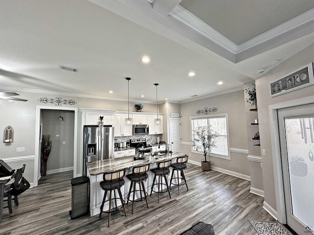 kitchen with crown molding, a center island with sink, a kitchen bar, stainless steel appliances, and white cabinetry