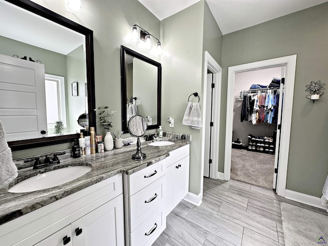 bathroom with double vanity, a spacious closet, baseboards, and a sink