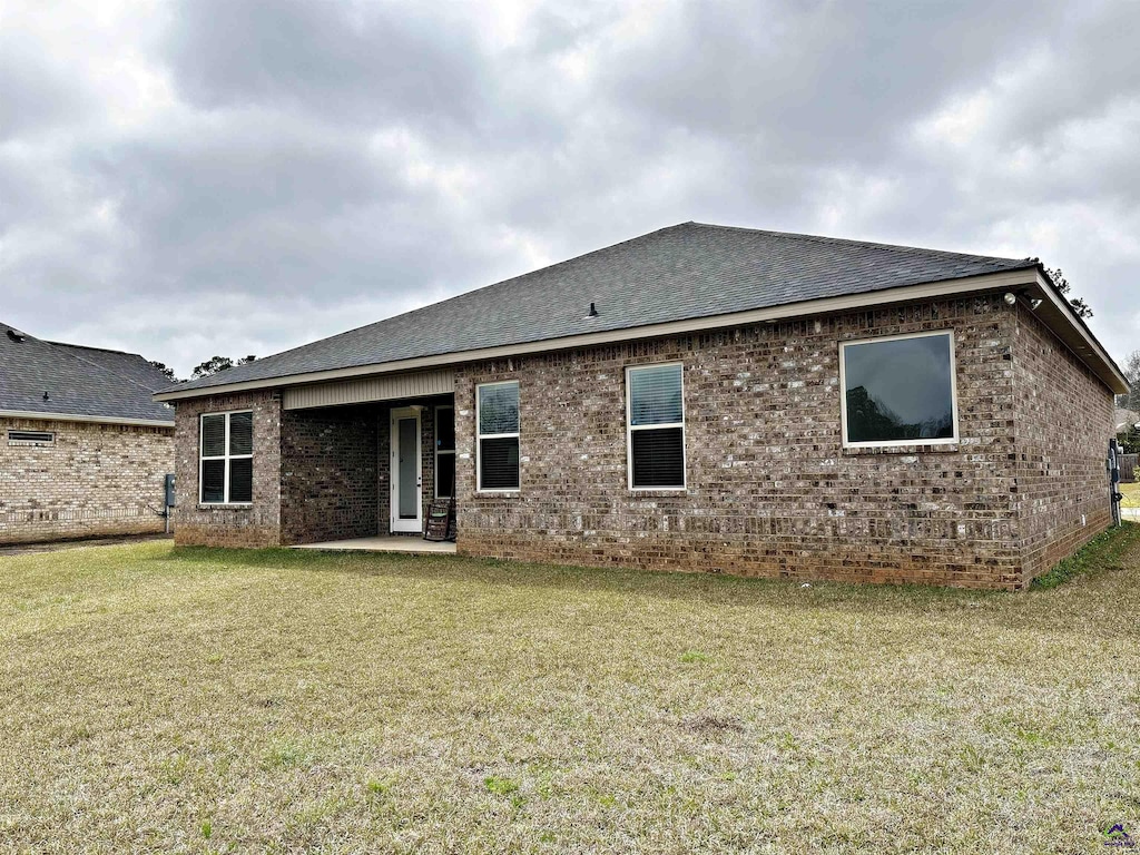 back of house with a patio area, a lawn, brick siding, and roof with shingles