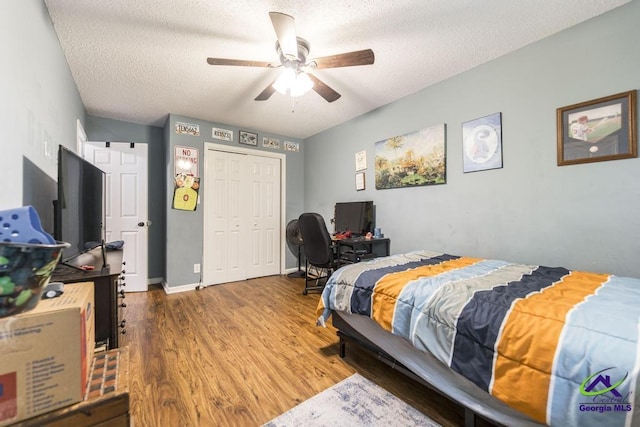 bedroom with a textured ceiling, wood finished floors, a closet, ceiling fan, and a desk
