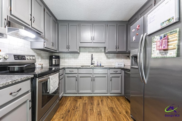 kitchen featuring stainless steel appliances, a sink, under cabinet range hood, gray cabinets, and a textured ceiling