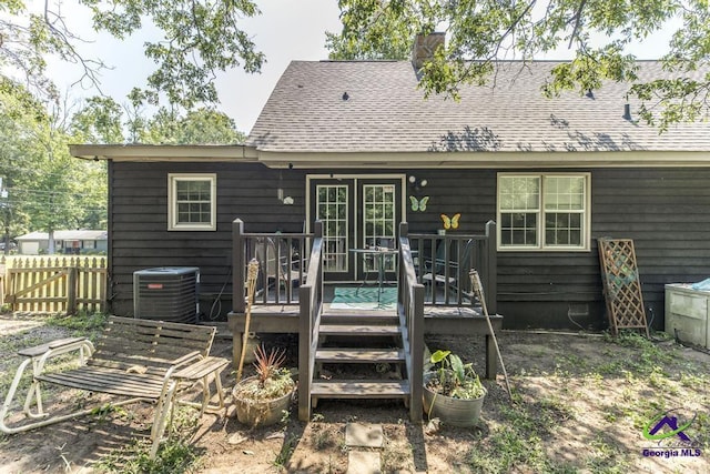 rear view of house featuring central AC, fence, a wooden deck, roof with shingles, and a chimney