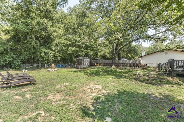 view of yard featuring an outdoor structure, a wooden deck, a trampoline, and a storage shed