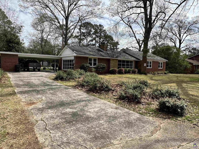 single story home with brick siding, an attached carport, concrete driveway, and a chimney
