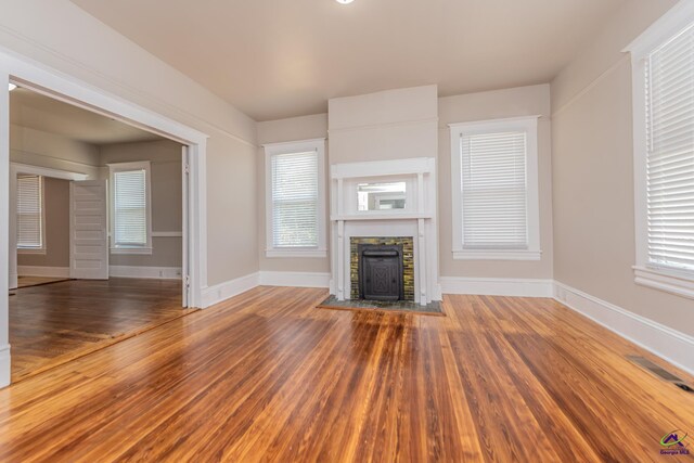 unfurnished living room with a fireplace, wood finished floors, visible vents, and baseboards
