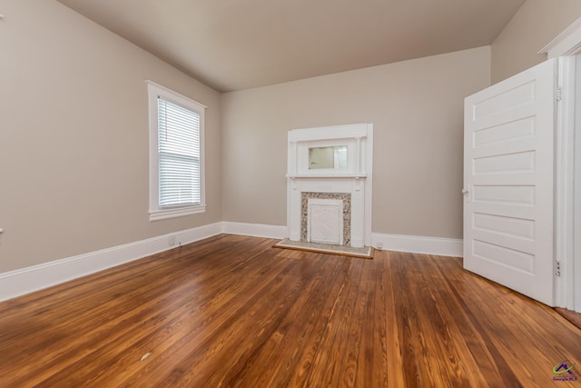 unfurnished living room featuring a fireplace with raised hearth, baseboards, and wood finished floors