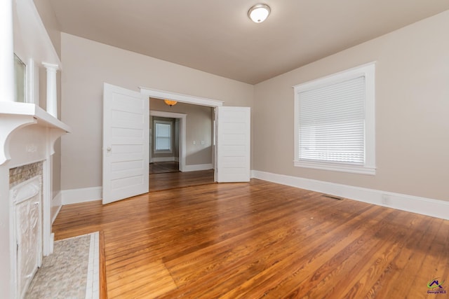 unfurnished living room featuring a fireplace with flush hearth, wood finished floors, and baseboards