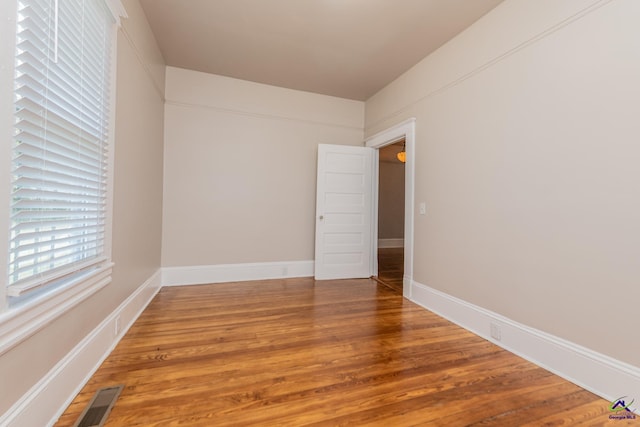 empty room featuring wood finished floors, visible vents, and baseboards