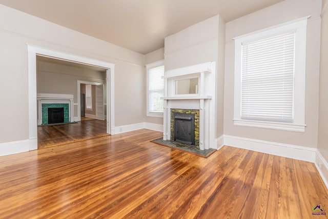 unfurnished living room with a fireplace with raised hearth, baseboards, and wood finished floors