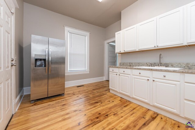 kitchen featuring baseboards, a sink, white cabinets, stainless steel refrigerator with ice dispenser, and light wood-type flooring