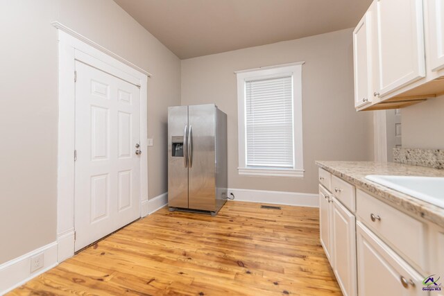 kitchen featuring white cabinetry, stainless steel fridge with ice dispenser, light wood-style floors, and baseboards