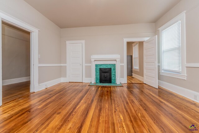 unfurnished living room featuring a fireplace with flush hearth, wood finished floors, and baseboards