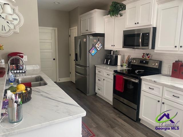 kitchen with tasteful backsplash, dark wood-type flooring, appliances with stainless steel finishes, white cabinets, and a sink