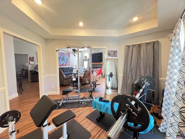 exercise room with a tray ceiling, a textured ceiling, wood finished floors, recessed lighting, and baseboards