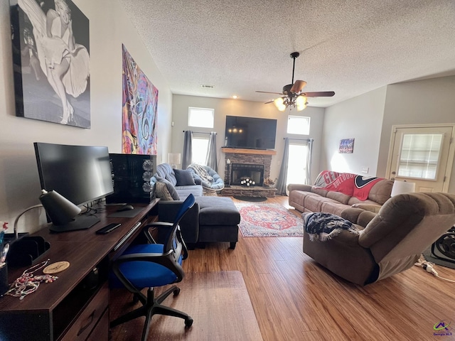 living area featuring visible vents, a ceiling fan, a textured ceiling, wood finished floors, and a fireplace