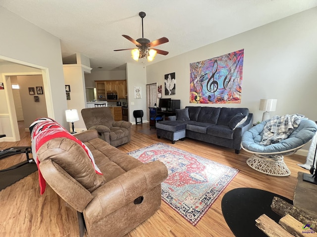 living area with vaulted ceiling, a ceiling fan, and light wood-type flooring