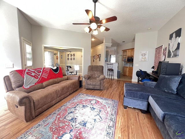 living area with ceiling fan, a textured ceiling, lofted ceiling, and light wood-style floors