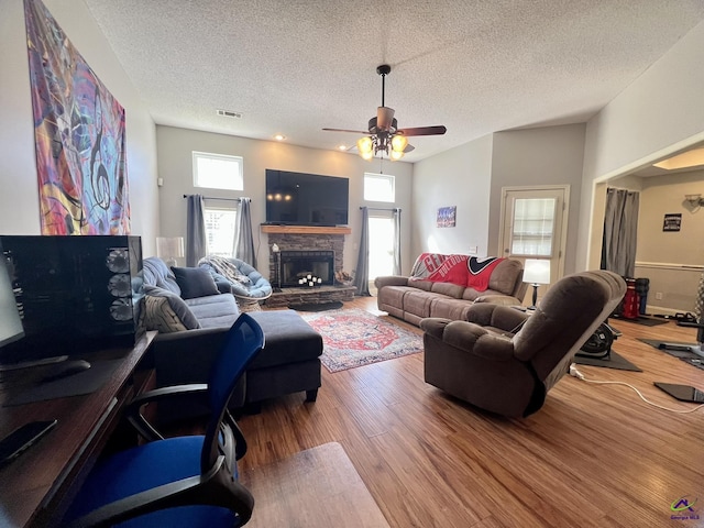 living area with visible vents, a stone fireplace, wood finished floors, a textured ceiling, and a ceiling fan