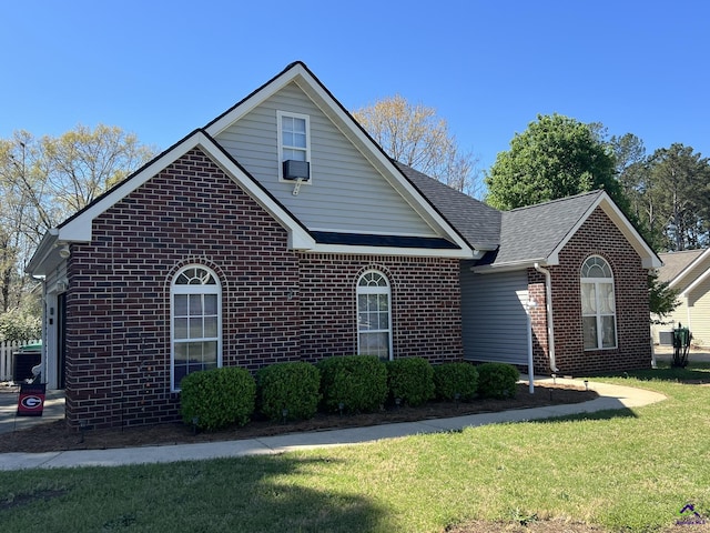 view of front of property with brick siding, a front lawn, and roof with shingles