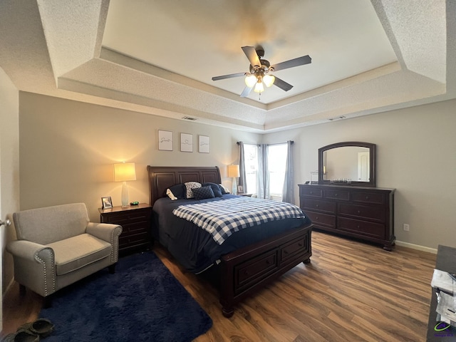 bedroom featuring visible vents, ceiling fan, baseboards, a tray ceiling, and wood finished floors