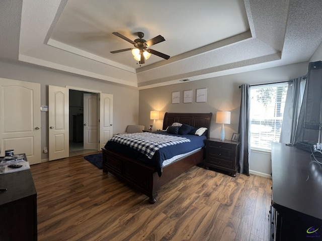 bedroom featuring visible vents, baseboards, a tray ceiling, and wood finished floors