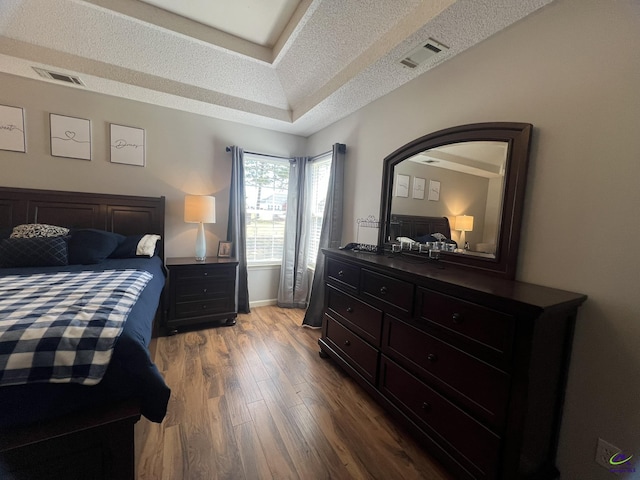bedroom with visible vents, a textured ceiling, a raised ceiling, and wood finished floors