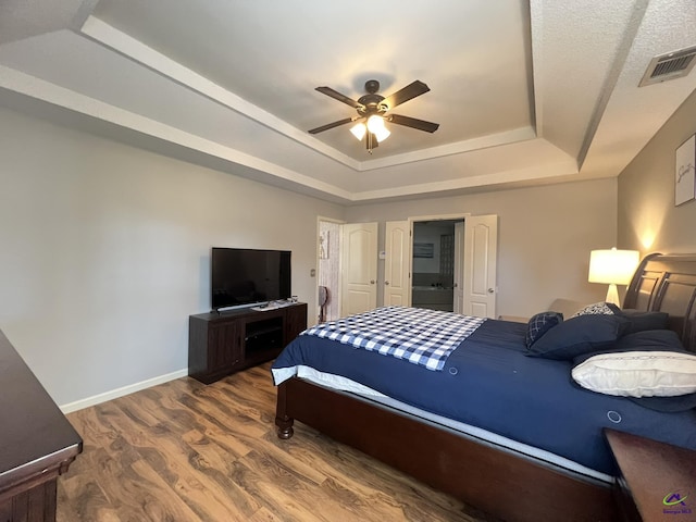 bedroom with a ceiling fan, wood finished floors, visible vents, baseboards, and a tray ceiling
