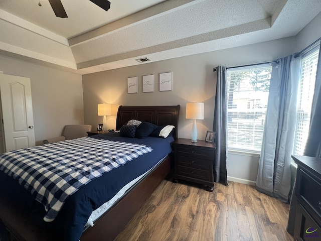 bedroom with visible vents, baseboards, a raised ceiling, and light wood-style floors
