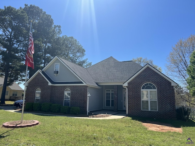 view of front of property with a front yard, brick siding, and a shingled roof