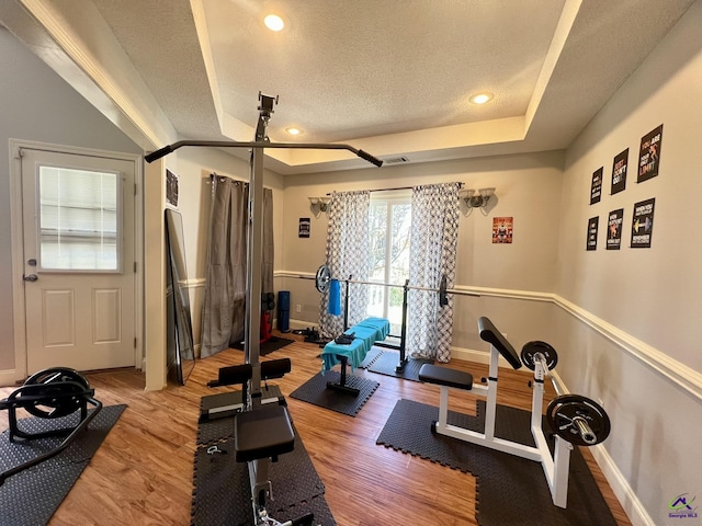 exercise area with visible vents, baseboards, light wood-style floors, a textured ceiling, and a raised ceiling