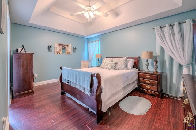 bedroom with dark wood finished floors, ceiling fan, a raised ceiling, and baseboards