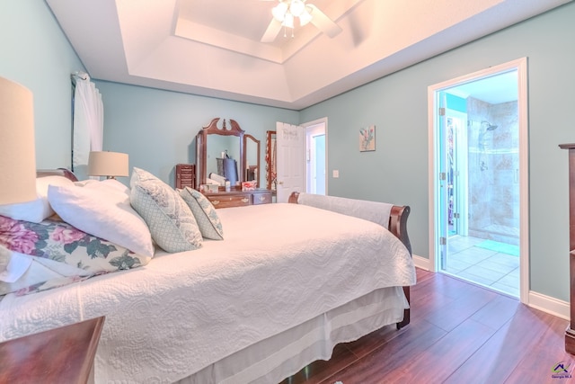 bedroom featuring a raised ceiling, ensuite bathroom, wood finished floors, baseboards, and ceiling fan