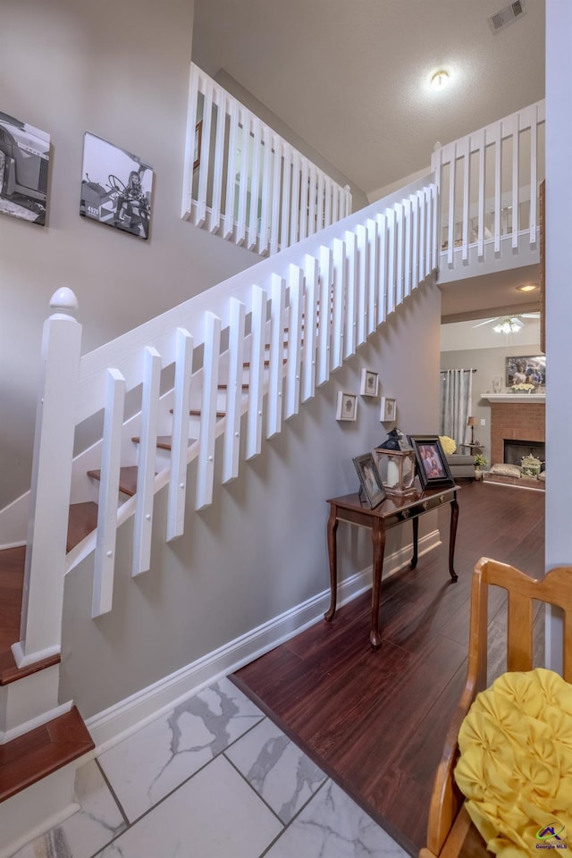 stairway featuring a fireplace, wood finished floors, visible vents, and baseboards