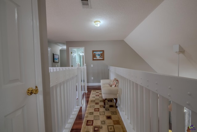 corridor featuring baseboards, visible vents, vaulted ceiling, a textured ceiling, and an upstairs landing