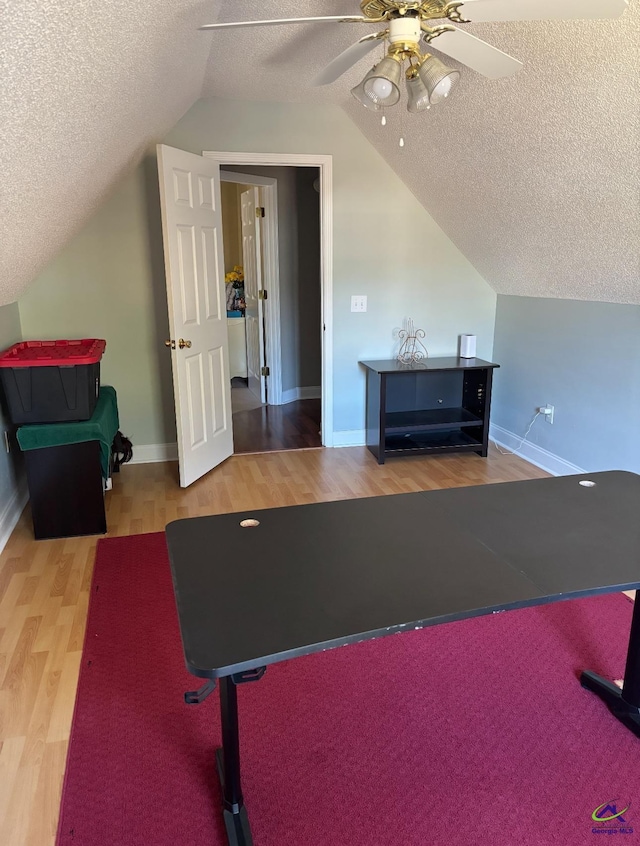 workout area with baseboards, vaulted ceiling, wood finished floors, a textured ceiling, and a ceiling fan