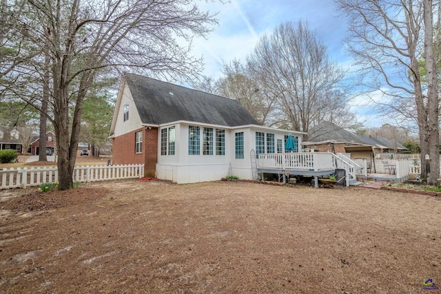 rear view of house with brick siding, a shingled roof, a deck, and fence