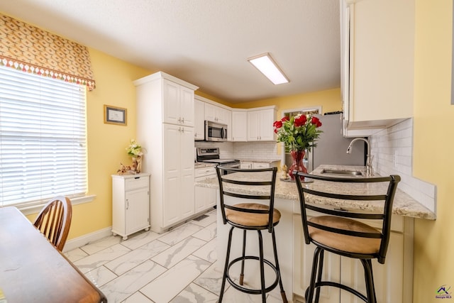 kitchen featuring a peninsula, a sink, appliances with stainless steel finishes, marble finish floor, and a wealth of natural light