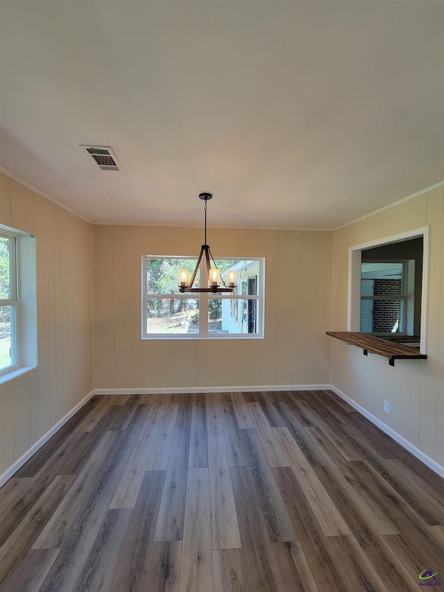 unfurnished dining area featuring crown molding, baseboards, a chandelier, visible vents, and wood finished floors