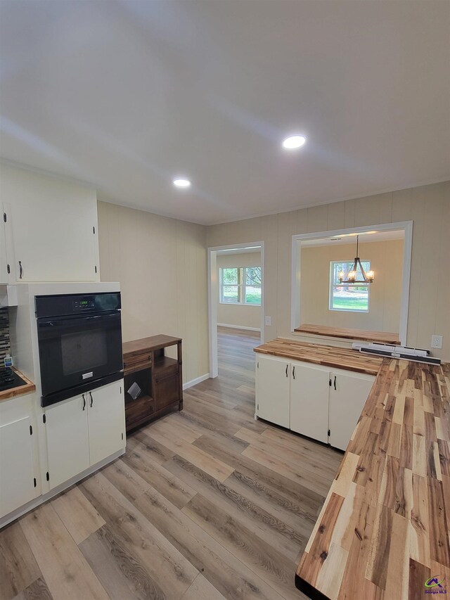 kitchen featuring white cabinets, wooden counters, light wood-style floors, black oven, and a notable chandelier