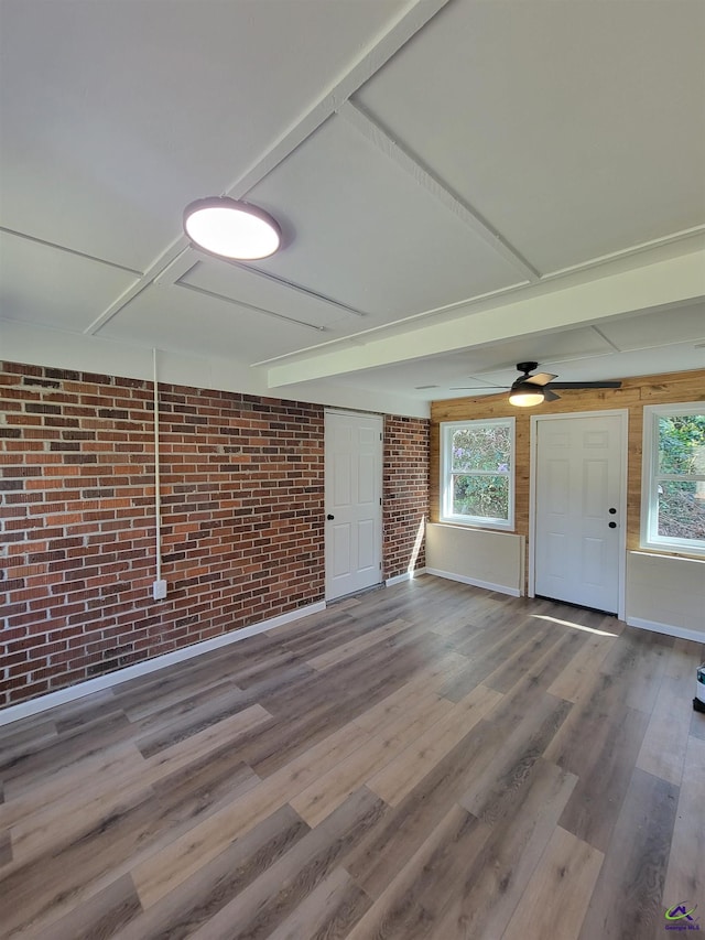 unfurnished living room with a ceiling fan, brick wall, and wood finished floors