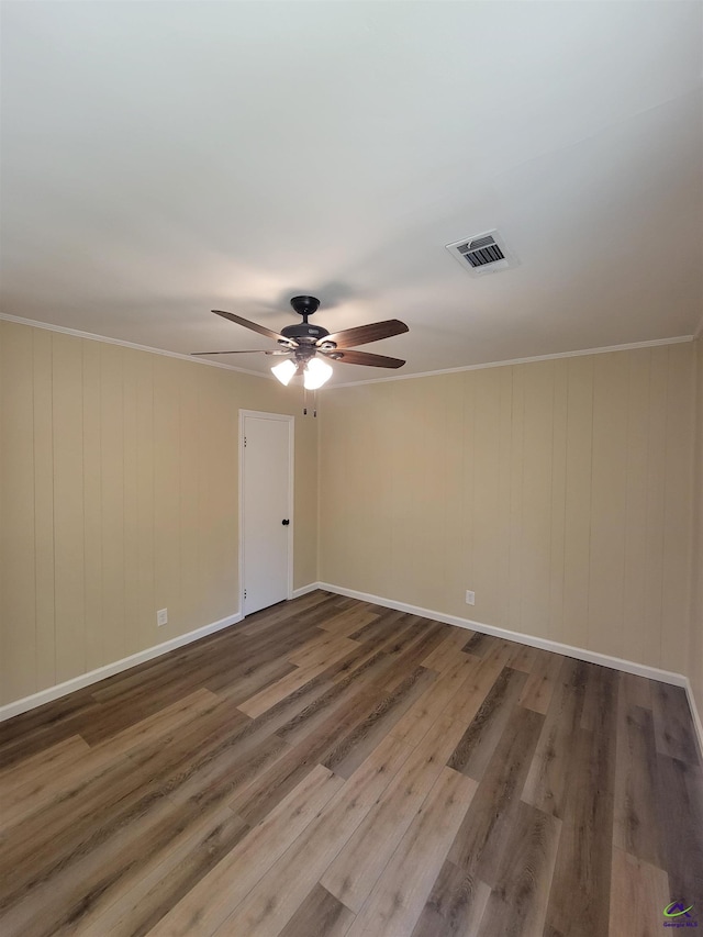 empty room with crown molding, wood finished floors, baseboards, visible vents, and ceiling fan