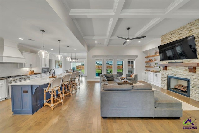 living area with a fireplace, ceiling fan, beam ceiling, light wood-type flooring, and coffered ceiling