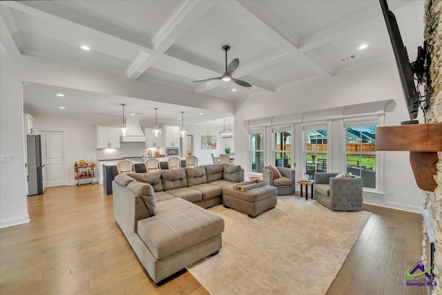 living room featuring a ceiling fan, light wood-style flooring, coffered ceiling, and beamed ceiling