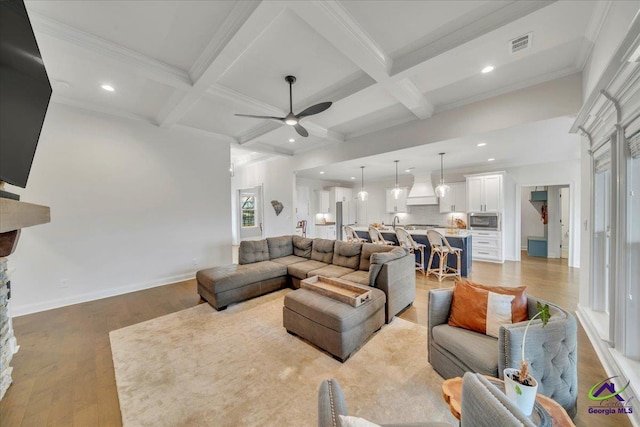 living area with baseboards, ceiling fan, light wood-style flooring, and beam ceiling