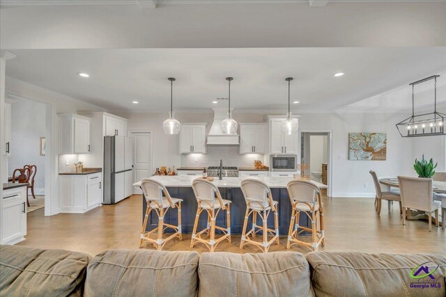 kitchen featuring white cabinetry, stainless steel microwave, backsplash, light wood finished floors, and freestanding refrigerator