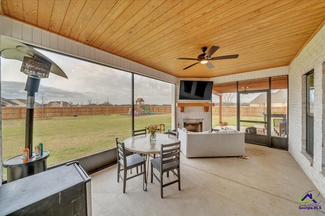 sunroom with a fireplace, outdoor dining space, and a ceiling fan