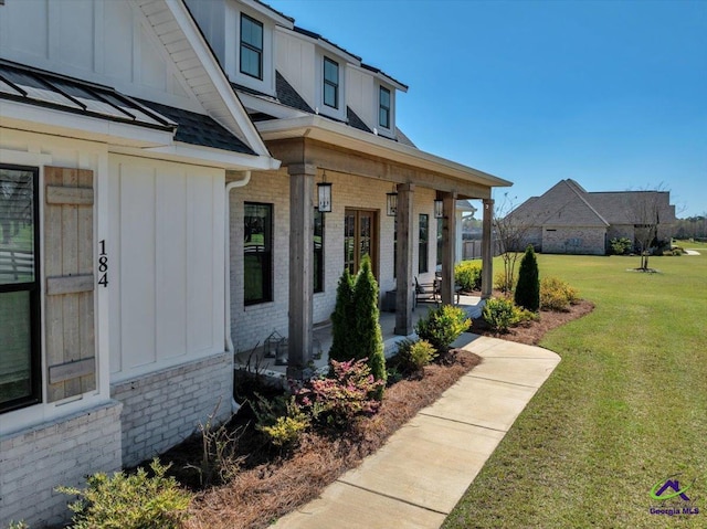 entrance to property featuring brick siding, a standing seam roof, board and batten siding, roof with shingles, and a yard