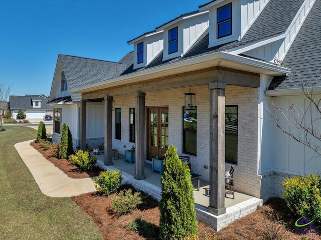 property entrance featuring french doors, board and batten siding, brick siding, and roof with shingles